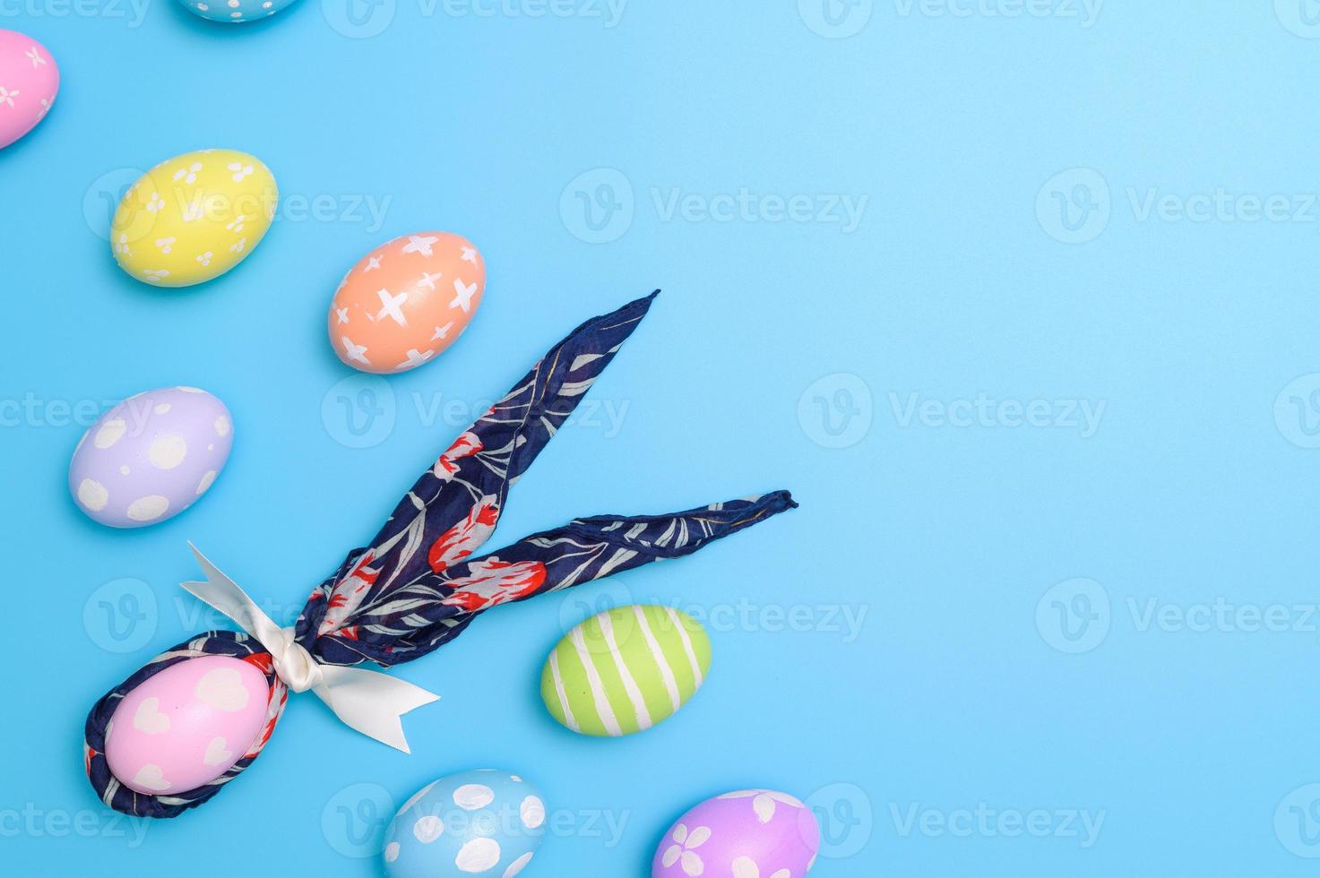 Happy Easter holiday greeting card design concept. Colorful Easter Eggs and spring flowers on blue background. Flat lay, top view, copy space. photo