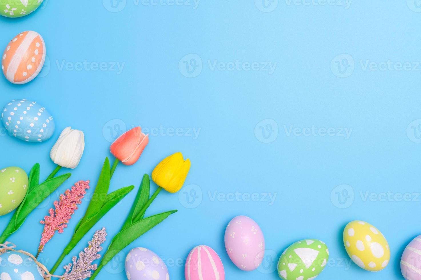 Happy Easter holiday greeting card design concept. Colorful Easter Eggs and spring flowers on blue background. Flat lay, top view, copy space. photo