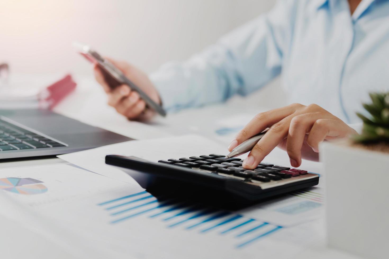 businesswoman working on desk using calculator laptop and mobile analyzing finance accounting in office photo