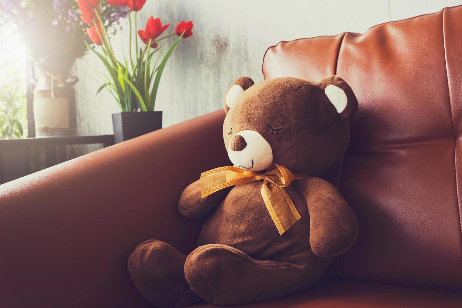bear doll on sofa with flower in vase photo