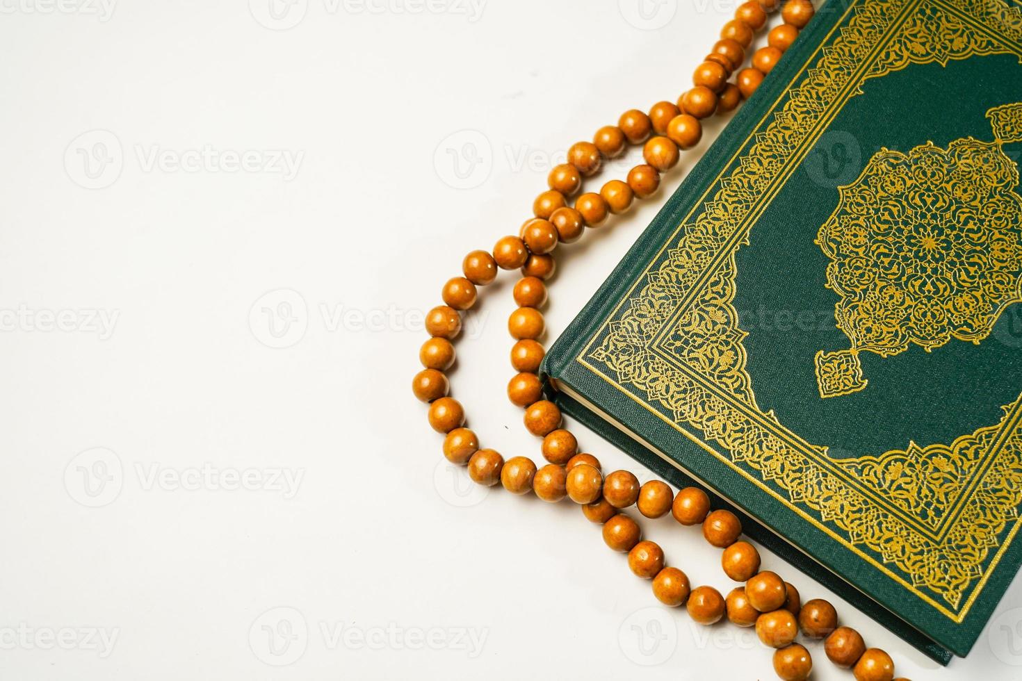 The Holy Al Quran with written arabic calligraphy meaning of Al Quran and rosary beads or tasbih on white background, isolated with copy space. photo