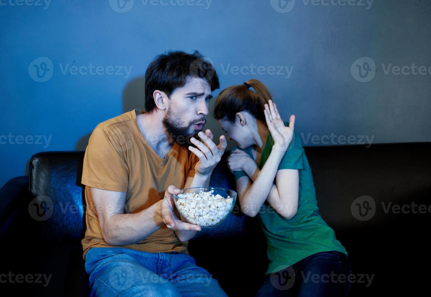 a man and a frightened woman watching a movie in the evening on the couch with a plate of popcor photo