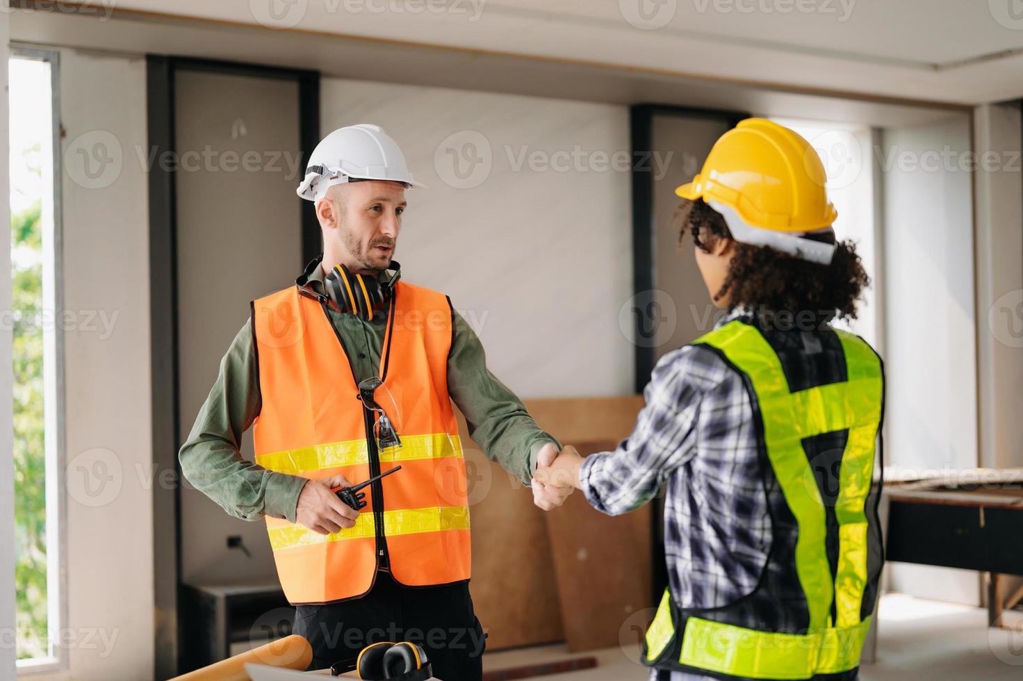 Construction team shake hands greeting start new project plan behind yellow helmet on desk in office center to consults about their building project. photo