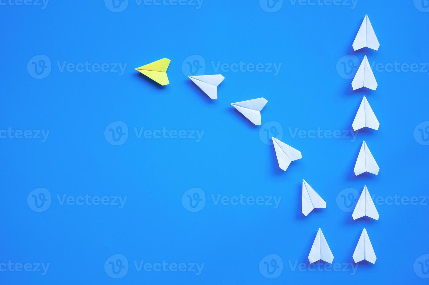 Top view of yellow paper airplane origami leading other white airplanes on blue background with customizable space for text or ideas. Leadership skills concept and copy space photo
