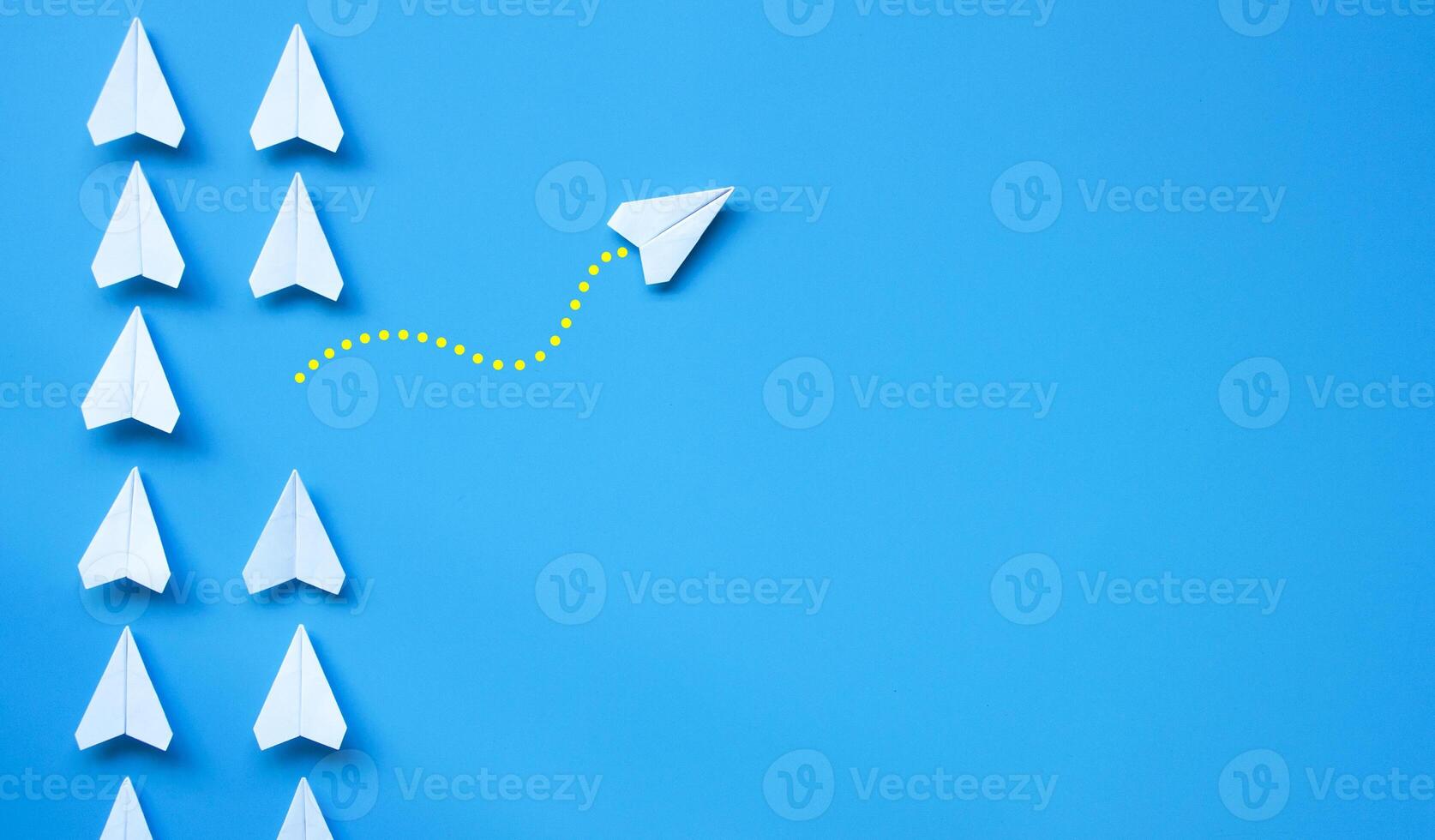 Top view of white paper airplane origami leaving other white airplanes on blue background with customizable space for text or ideas. Leadership skills concept and copy space photo