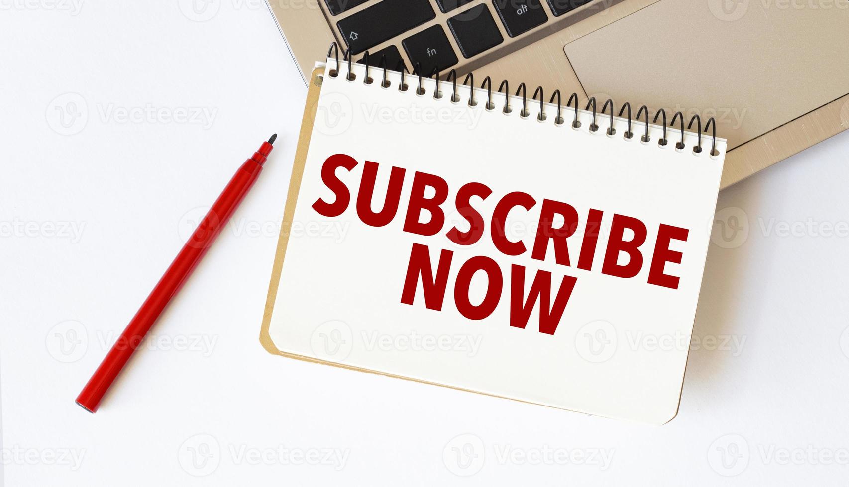 Laptop, red pen and notepad with text subscribe now in the white background photo