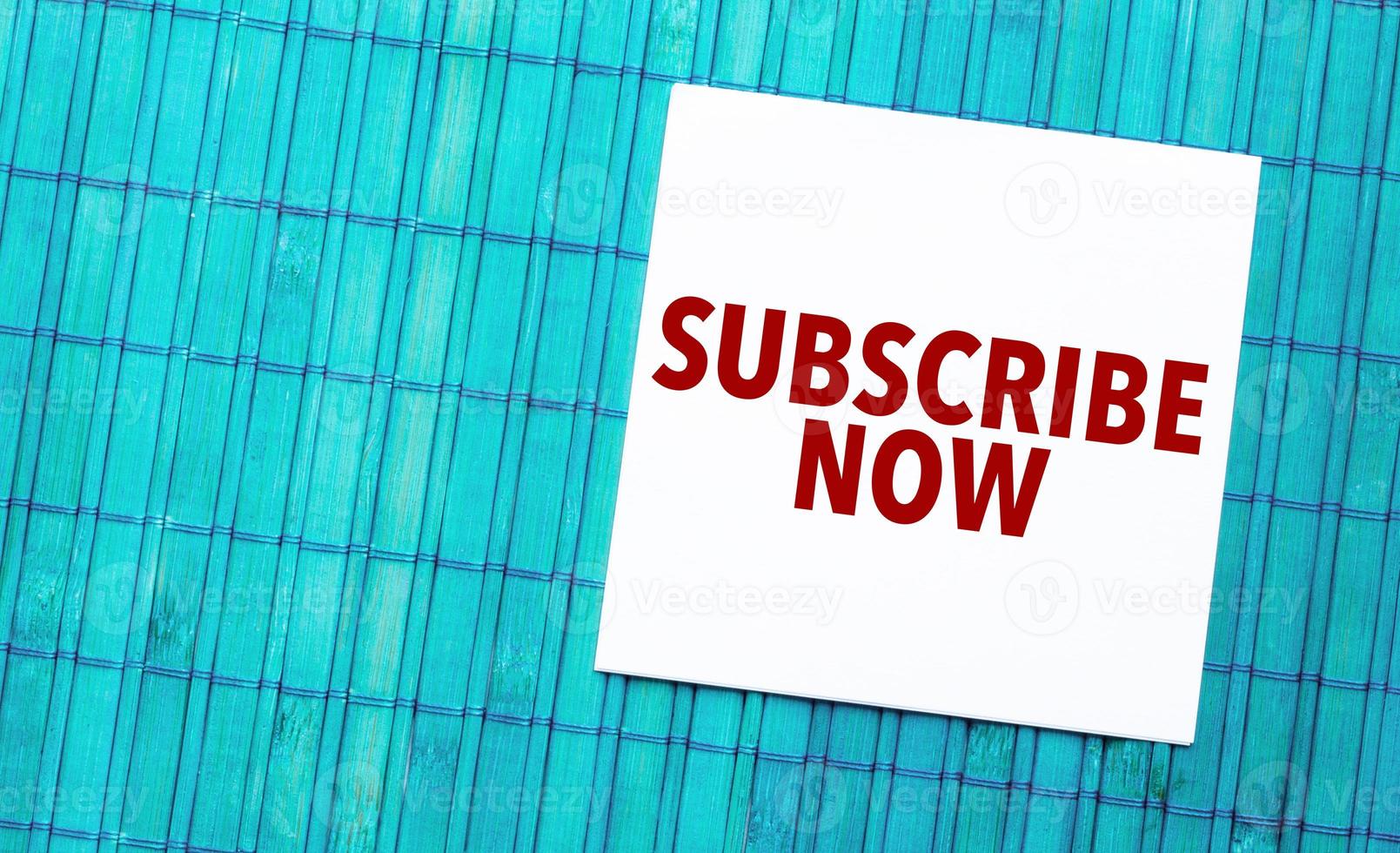 subscribe now word on torn paper with blue wooden background photo