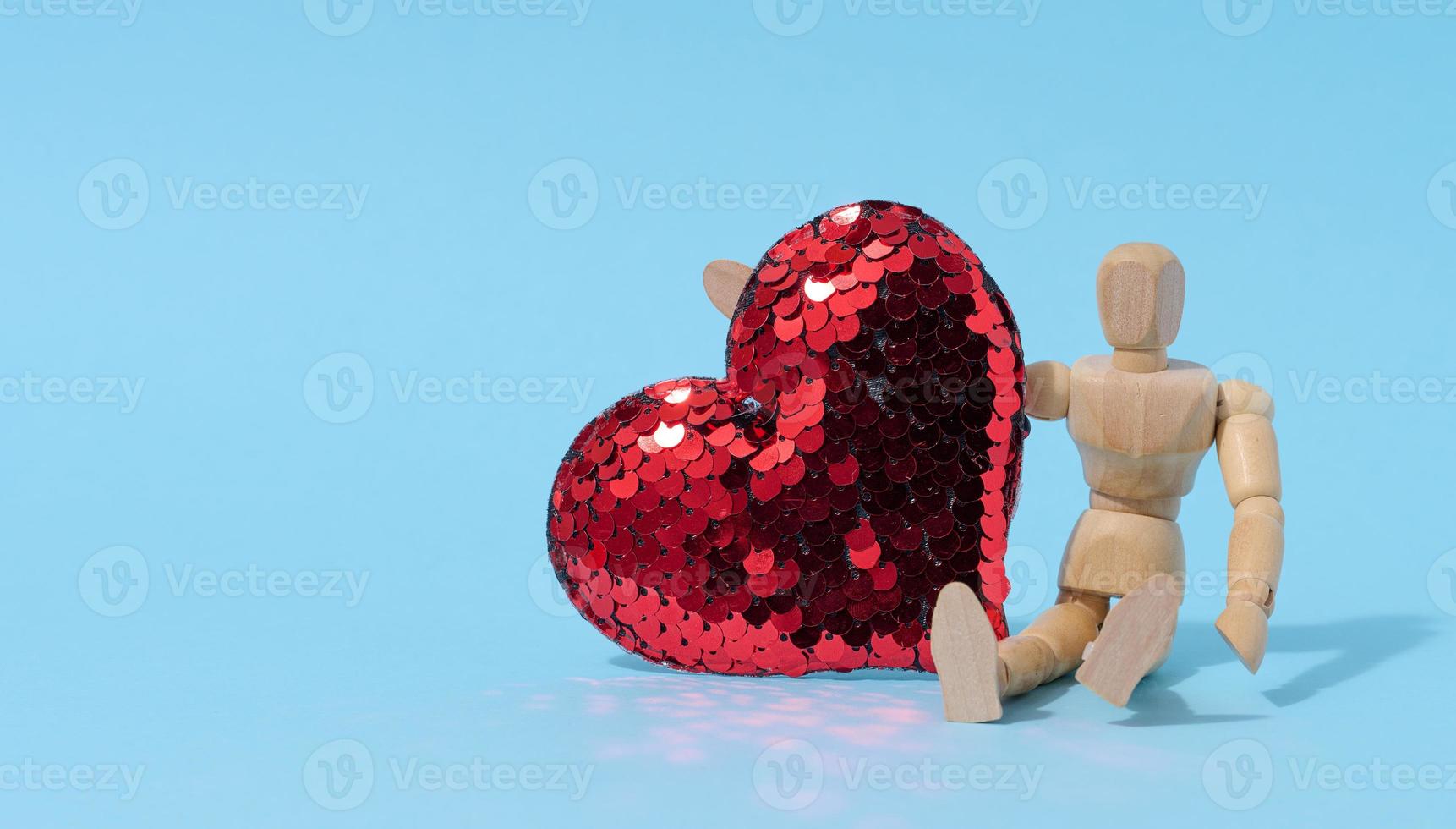 Wooden mannequin and red heart made of sequins on a blue background photo