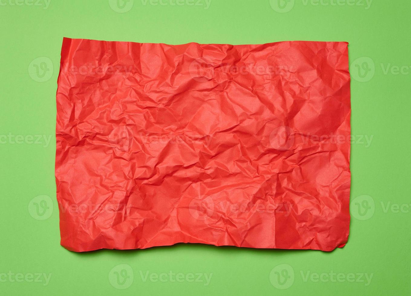 Crumpled rectangular sheet of red paper on a green background, top view. Place for inscription photo