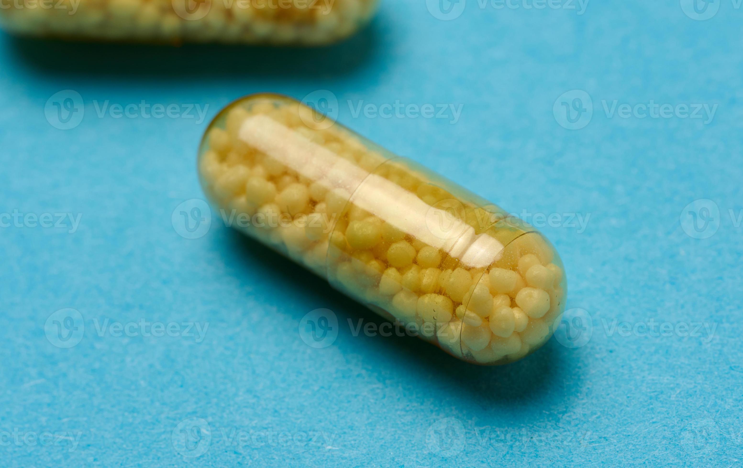 Transparent medical capsules with yellow granules inside on a blue background, tablets for