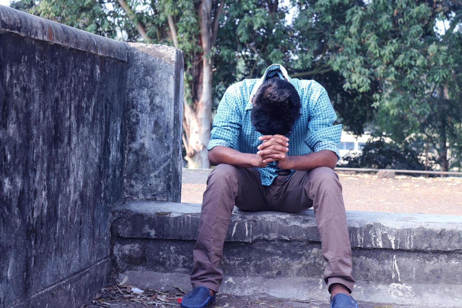 Rangpur, Bangladesh 2023. Depressed Teenager man sitting alone on Wall in Outdoor.Unpleasant pain. Sad unhappy handsome man.Bangladeshi and Asia boy Suffering Depression. photo