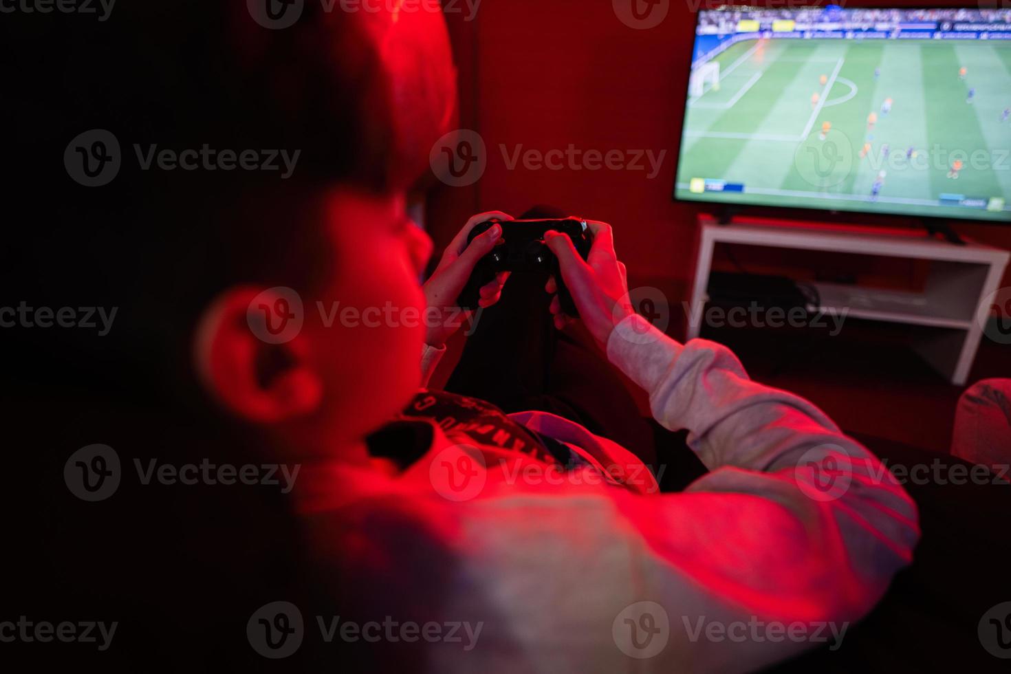 Teenager boy gamer play football gamepad video game console in red gaming room. photo