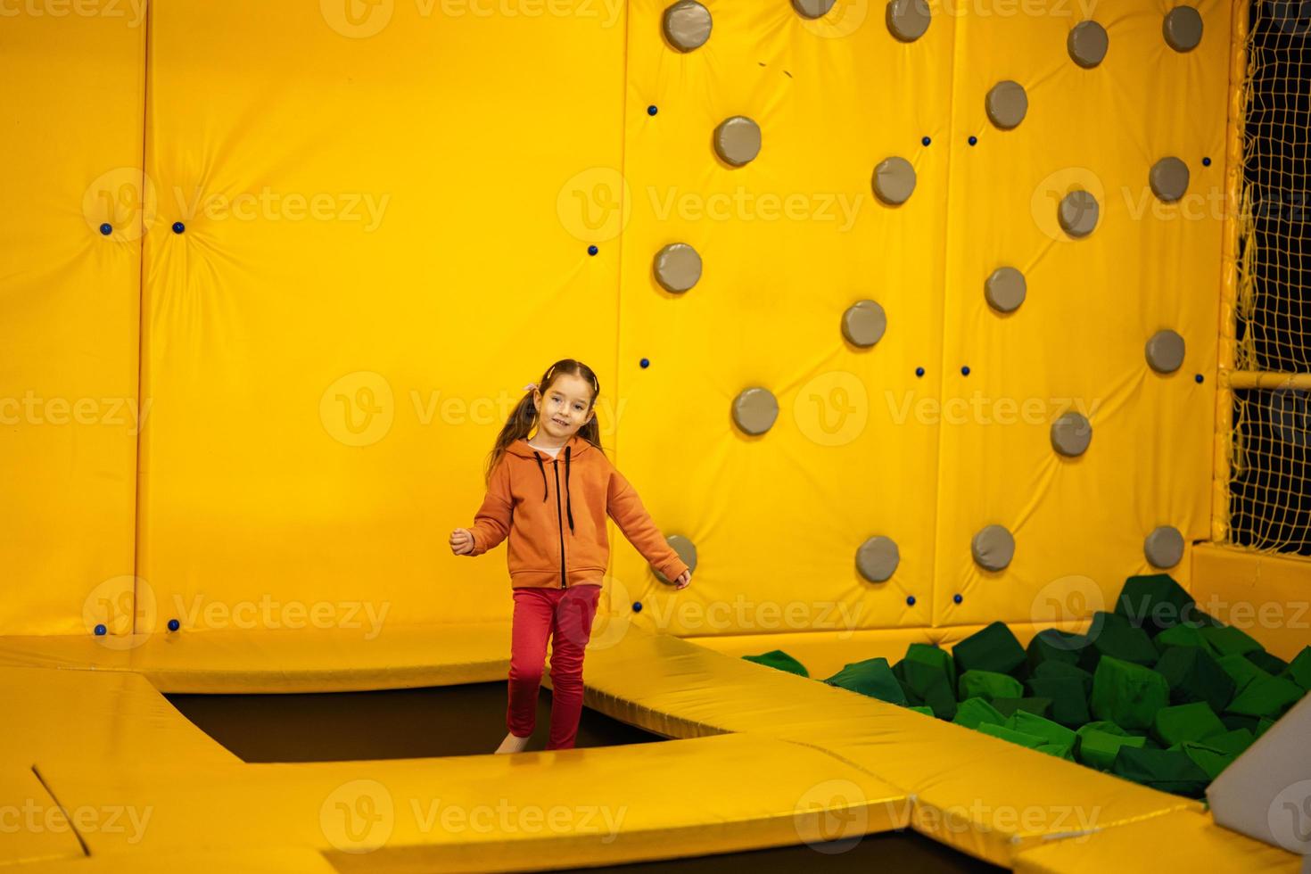Little girl kid jumping on trampoline at yellow playground park. Child in motion during active entertaiments. photo