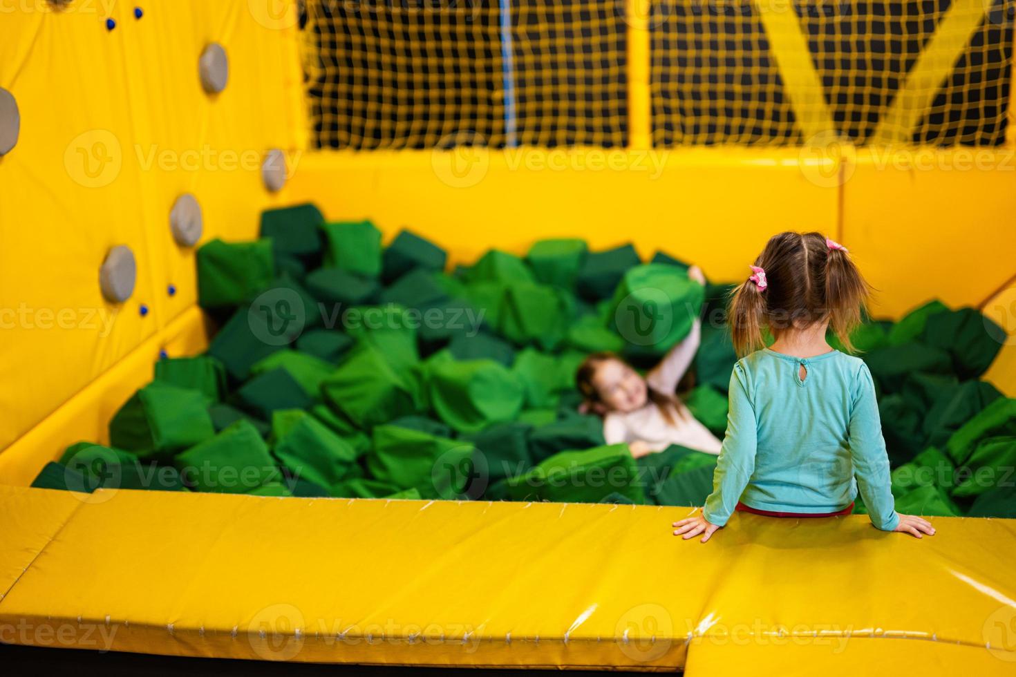 Little girl kid lies on green soft cubes at playground park. Child in active entertaiments. photo