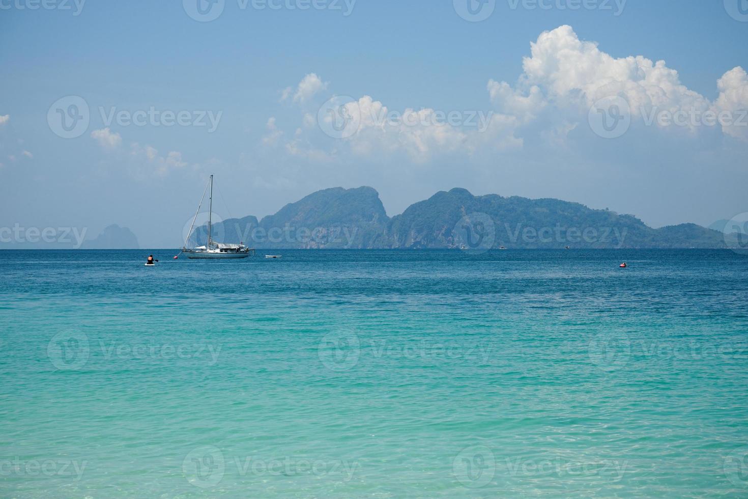 The yacht parking in the calm sea with moving paddle boat and mountain with blue sky in background photo