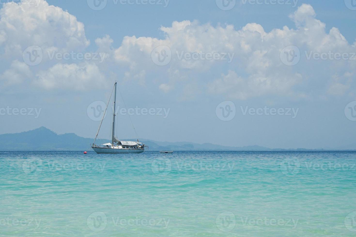 The yacht parking in the calm sea with moving paddle boat and mountain with blue sky in background photo