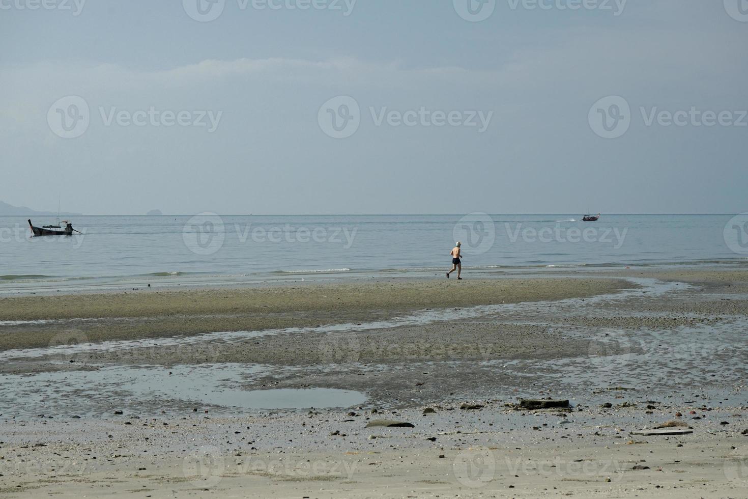 Healthy man runs alone along the beach with horizontal line of seascape and parking boats in background photo