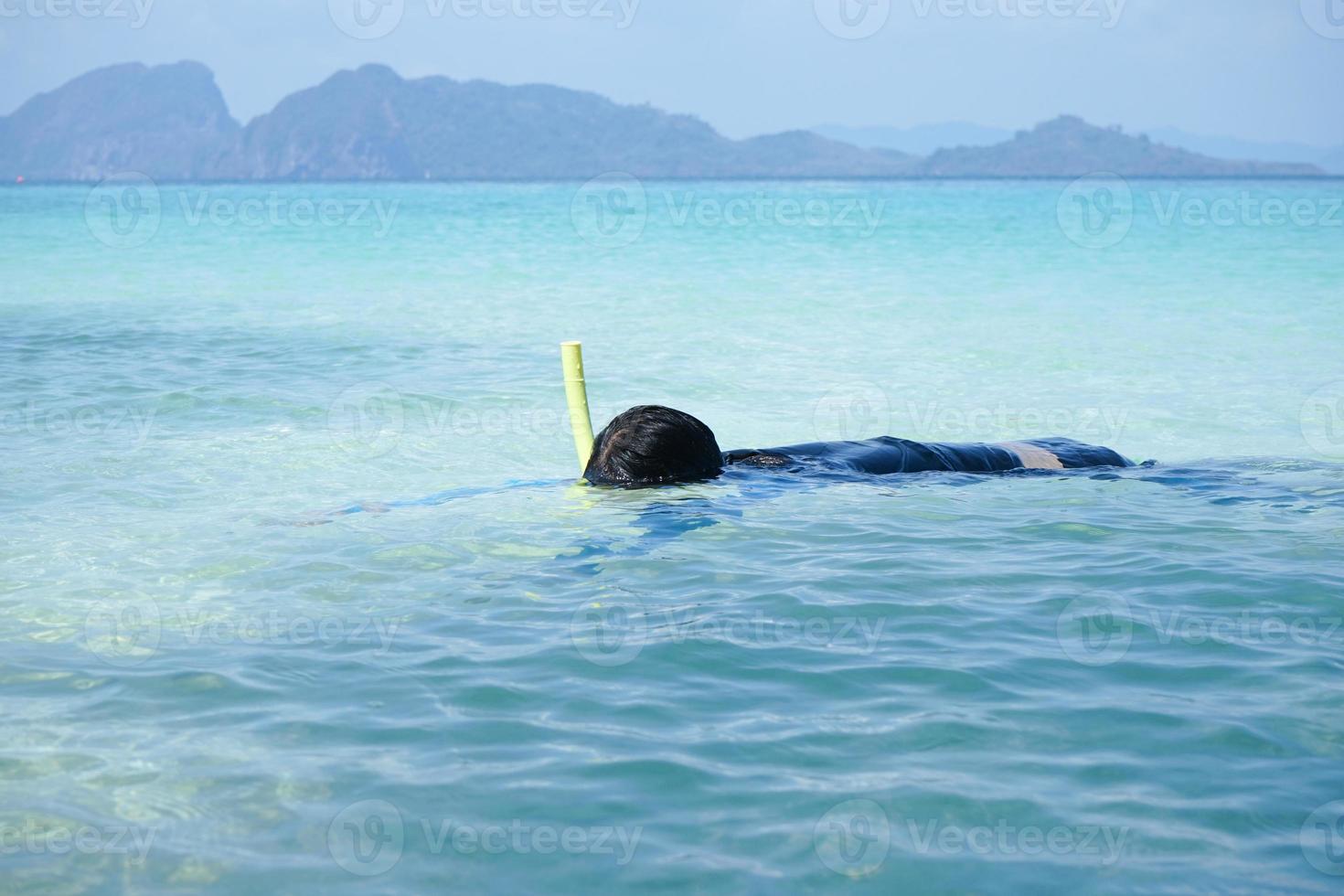 A girl is floating on the surface of the sea and sees the reef and fish under the water by snorkel mask photo