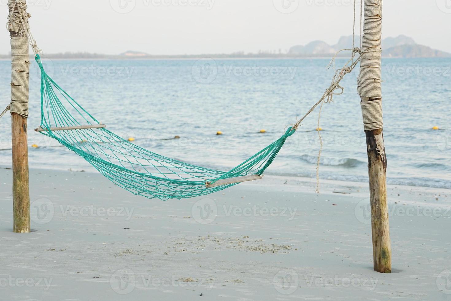 Empty swing weaved by rope hanging on the wooden poles on the beach with seascape background photo