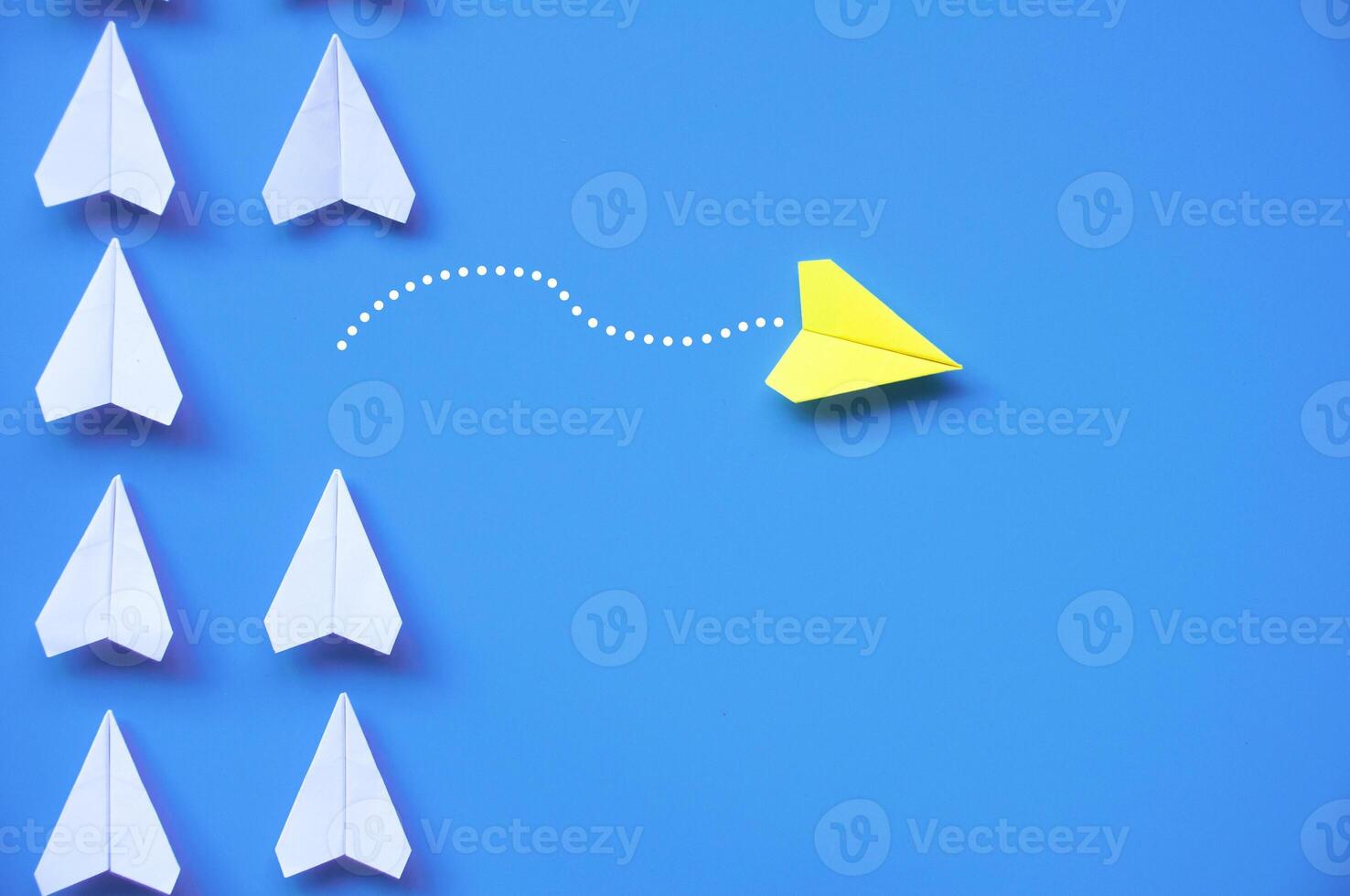 Yellow paper airplane origami leaving other white airplanes on blue background with customizable space for text or ideas. Leadership skills concept and copy space photo