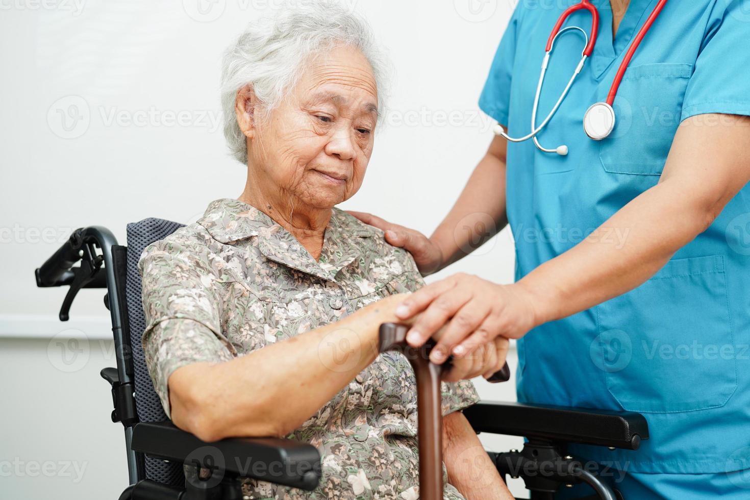 Doctor help Asian elderly disability woman patient holding walking stick in wrinkled hand at hospital. photo