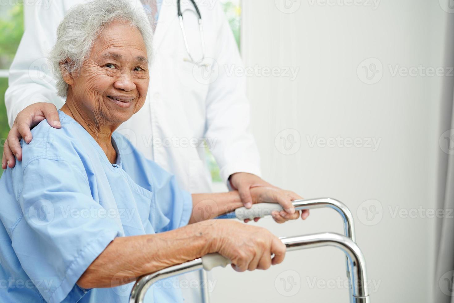Doctor help Asian elderly woman disability patient walk with walker in nursing hospital, medical concept. photo