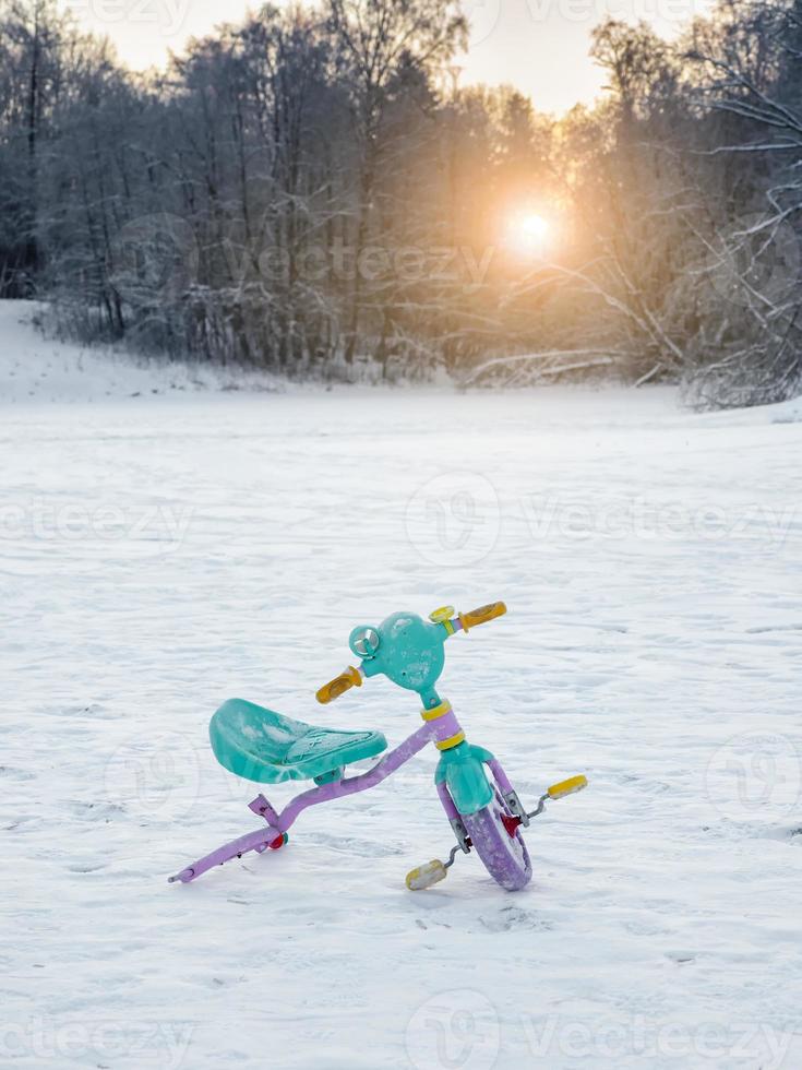 Abandoned broken children's bike in the snow. The end of the holidays. photo