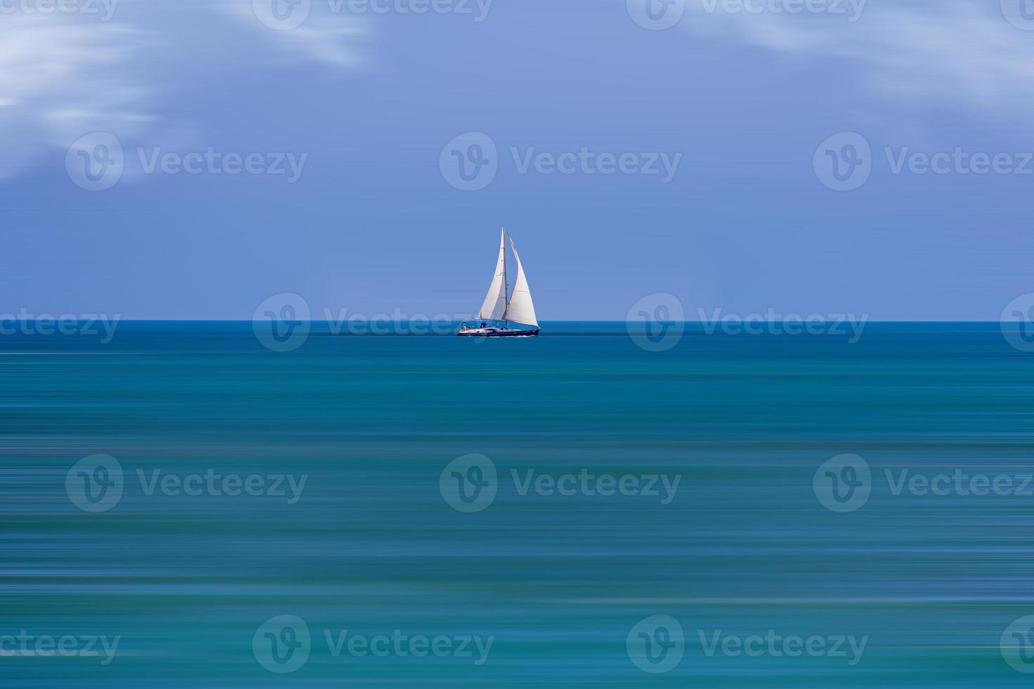 calm sea landscape with white sailboat against blue sky and long water time photo