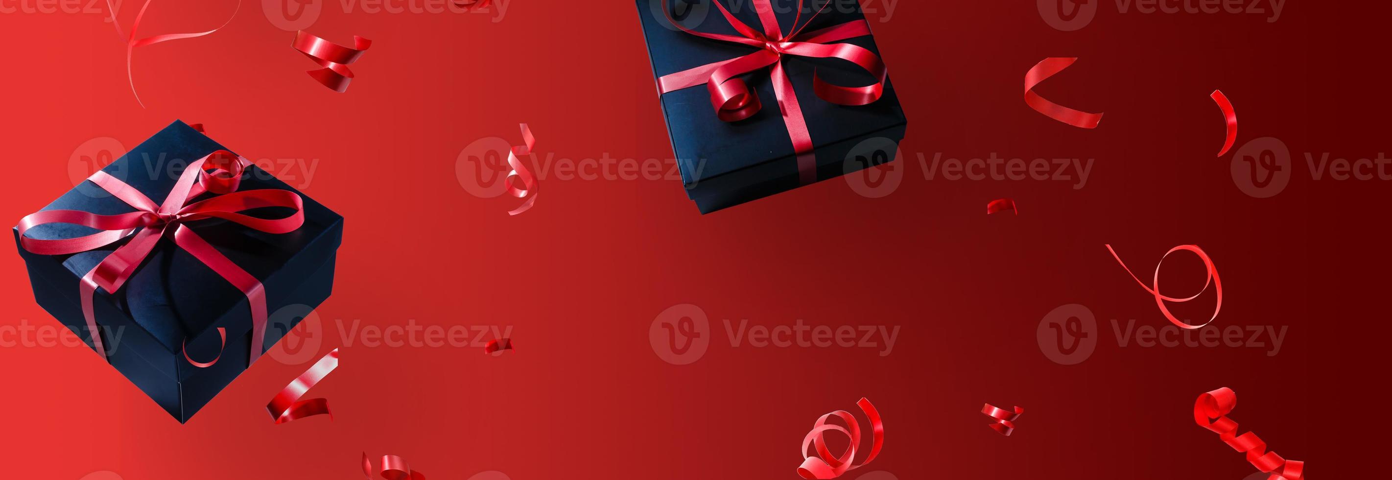 Black gift box with red ribbon and bow, over red background. photo