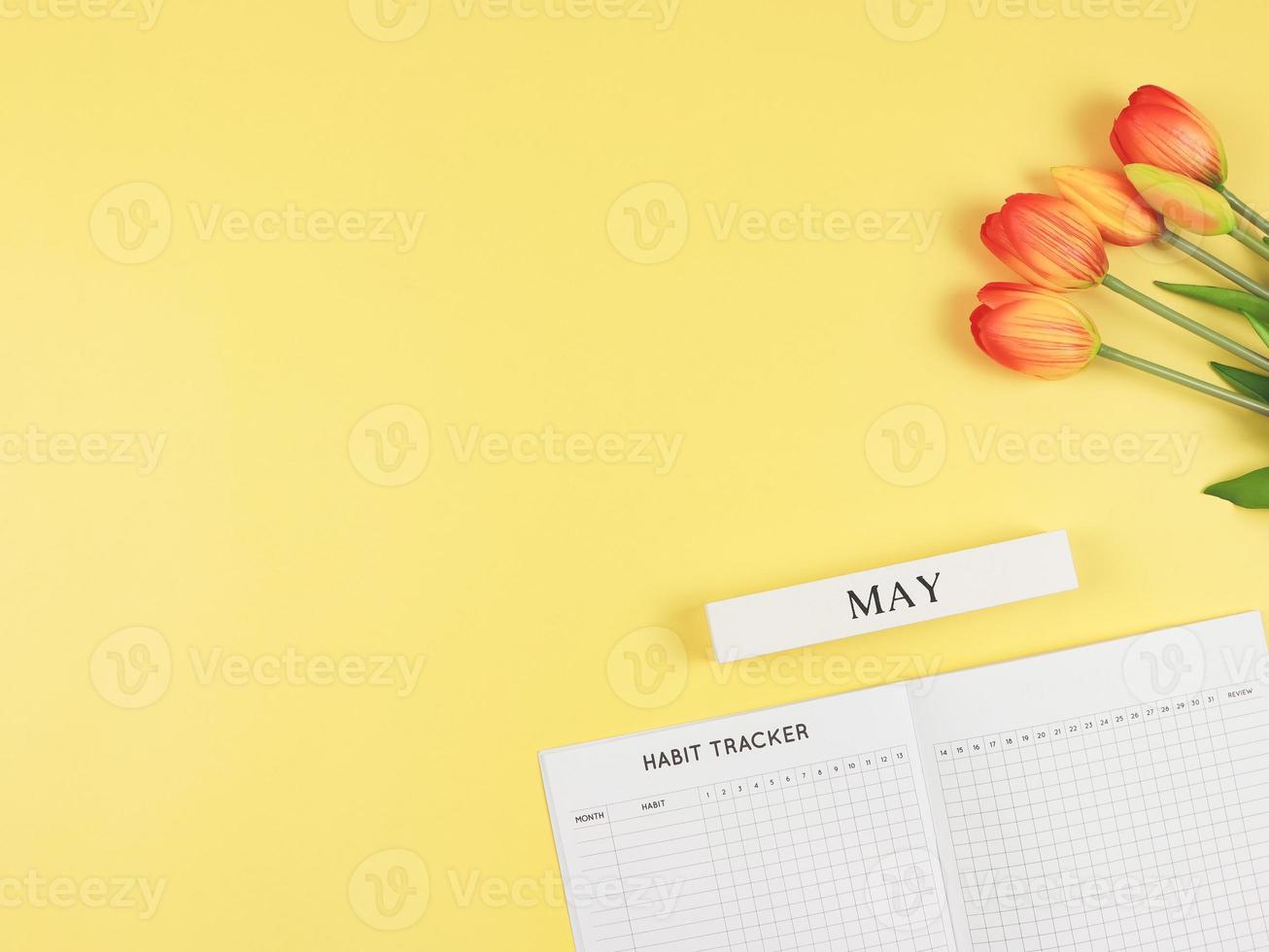 flat layout of Habit tracker book, wooden calendar May,  and tulips on yellow background with copy space. photo