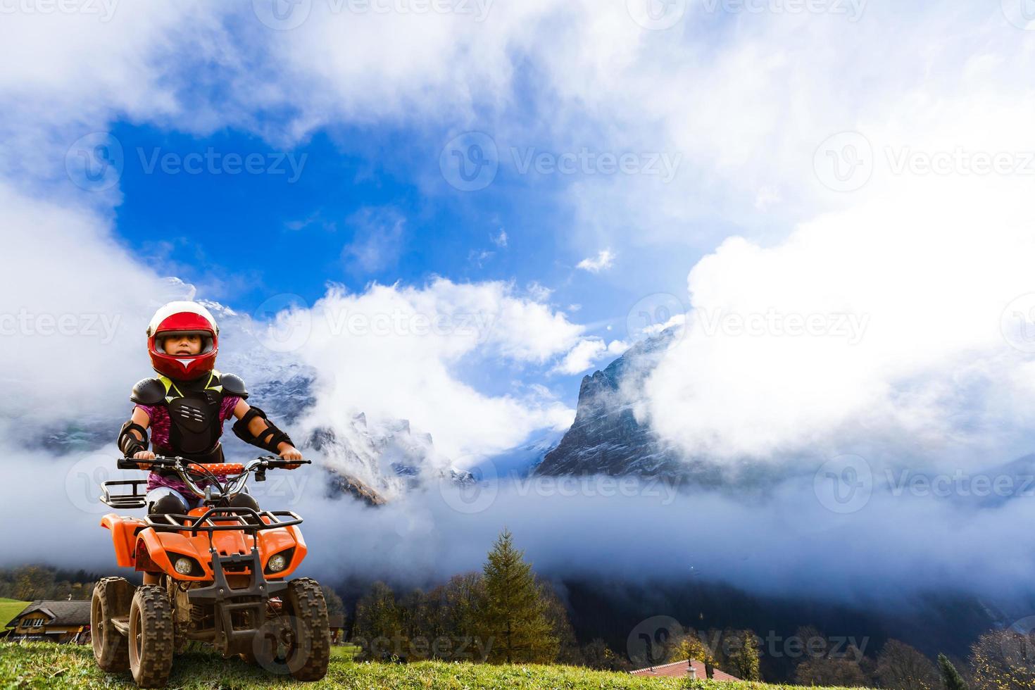 Girl riding quad bike mountain, ATV. Cute child on quadricycle. Kids summer vacation activity. photo