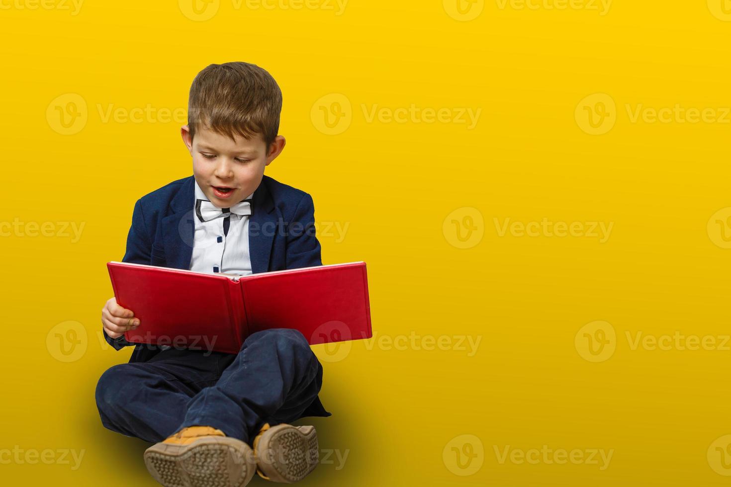 A little boy reading a big book. Isolated on yellow background photo