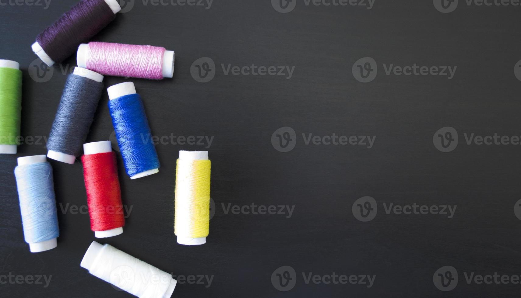 sewing threads  on a dark wood background, spools of thread, multi colored thread, sewing accessories, top view photo