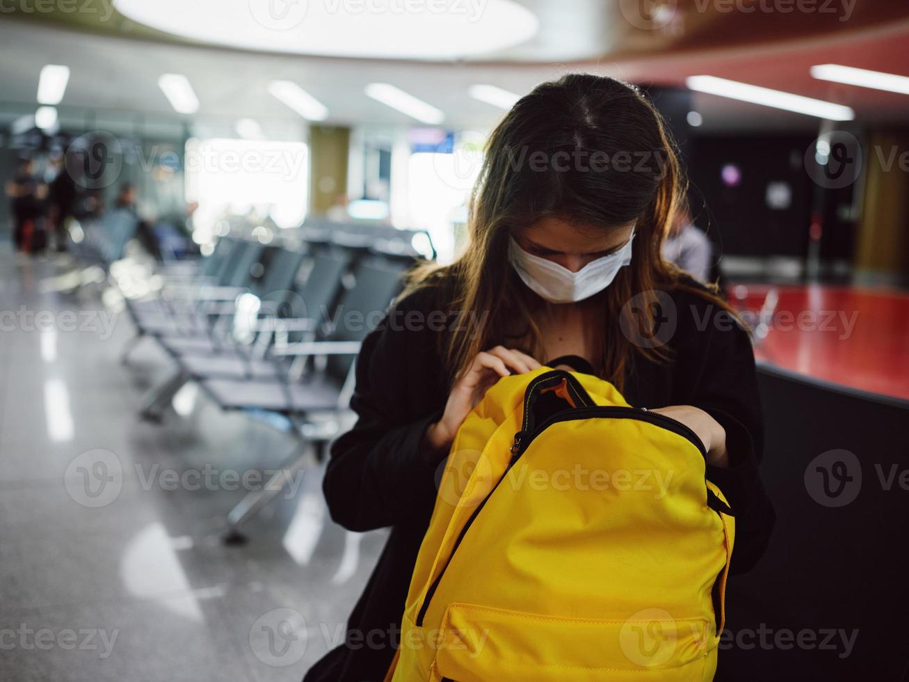 a passenger in a medical mask at the airport looks into a yellow backpack photo