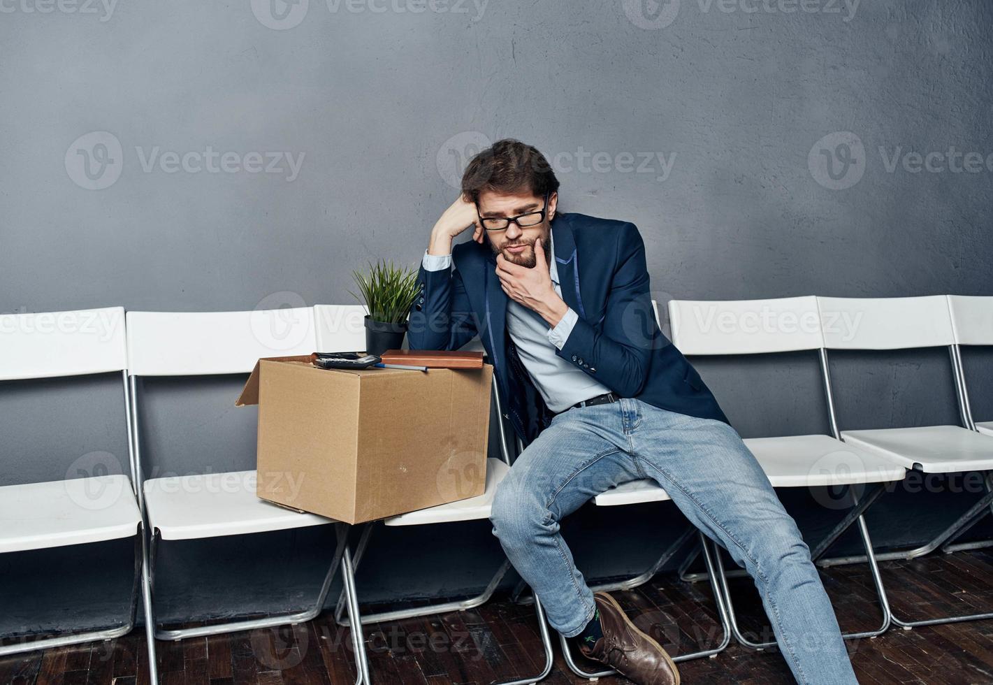 disgruntled man sitting on chairs with a box job search photo