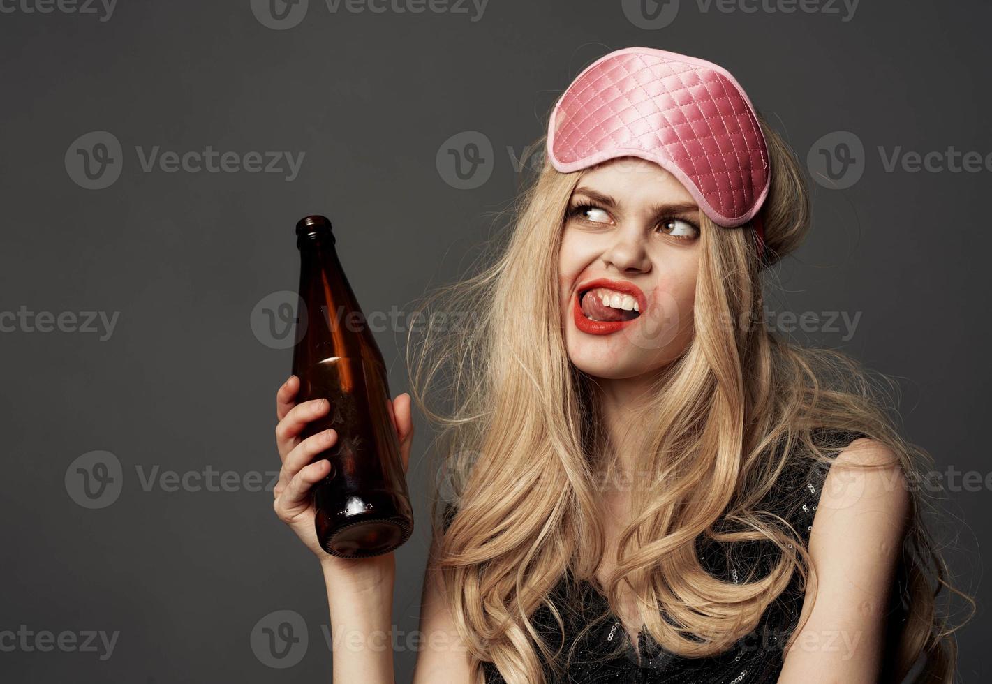 Angry woman with a bottle of beer in her hand with bright makeup and a pink sleep mask photo