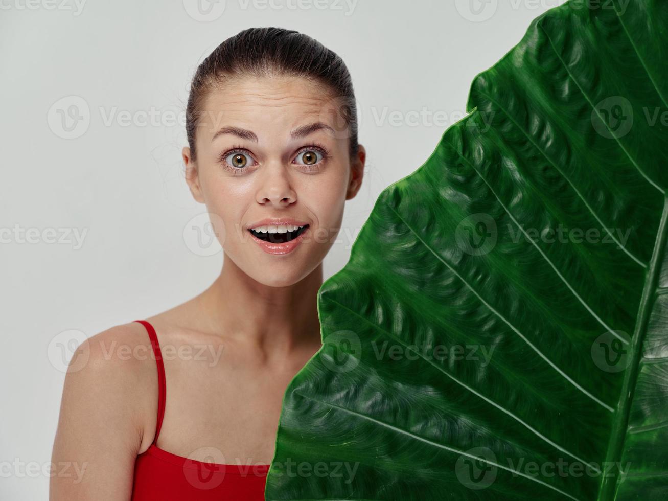 surprised woman with wide open mouth stands behind green palm leaf photo