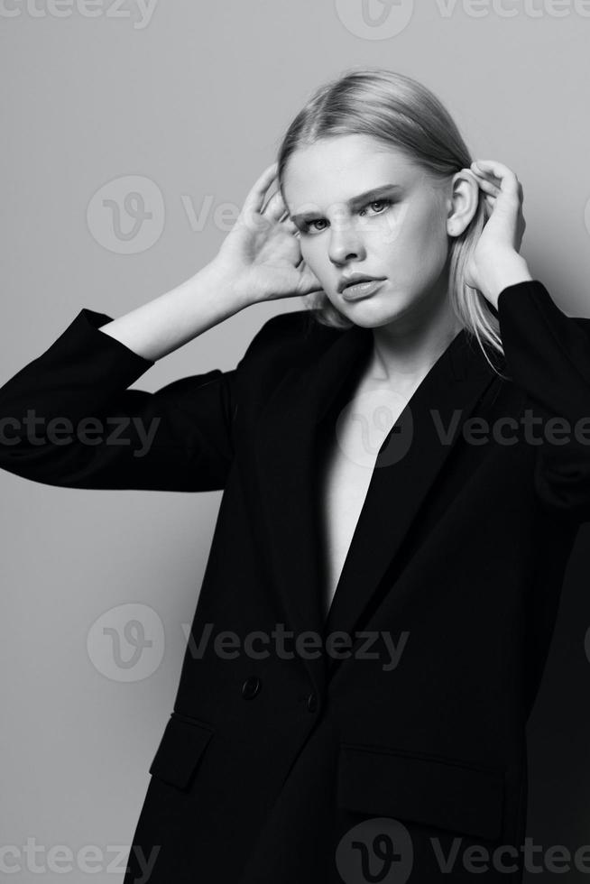 Elegant girl puts her hand to her face tucks her hair behind her ear poses in the studio in black and white style photo