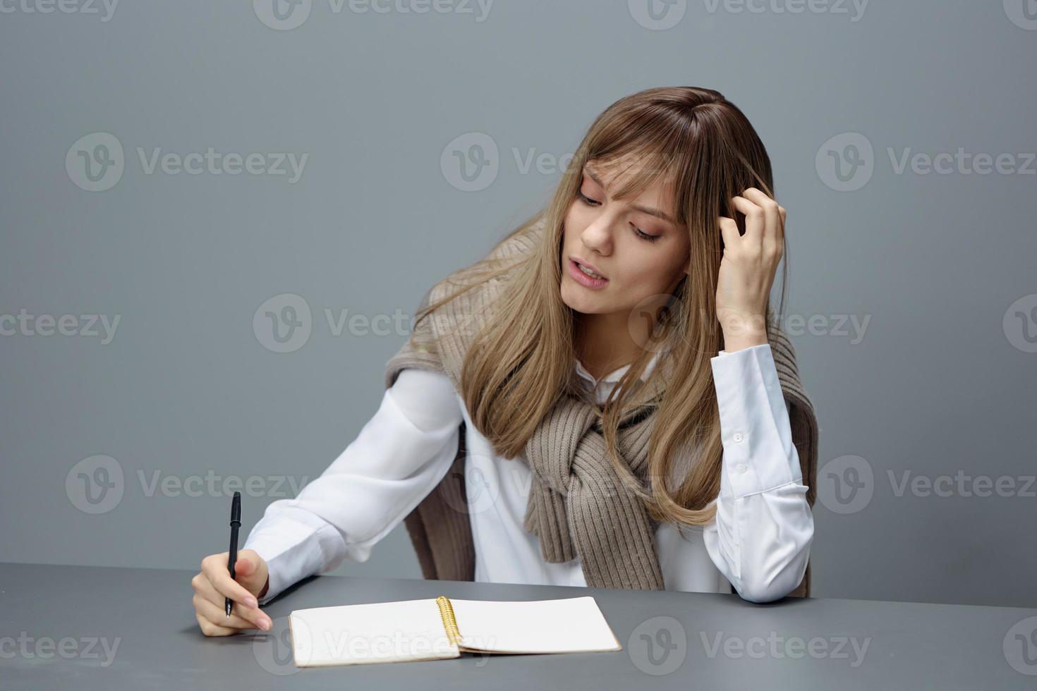 triste cansado joven rubia estudiante dama persona de libre dedicación en calentar suéter haciendo deberes sentado a lugar de trabajo en gris moderno hogar oficina. remoto trabajo, educación y carrera profesión concepto. Copiar espacio foto