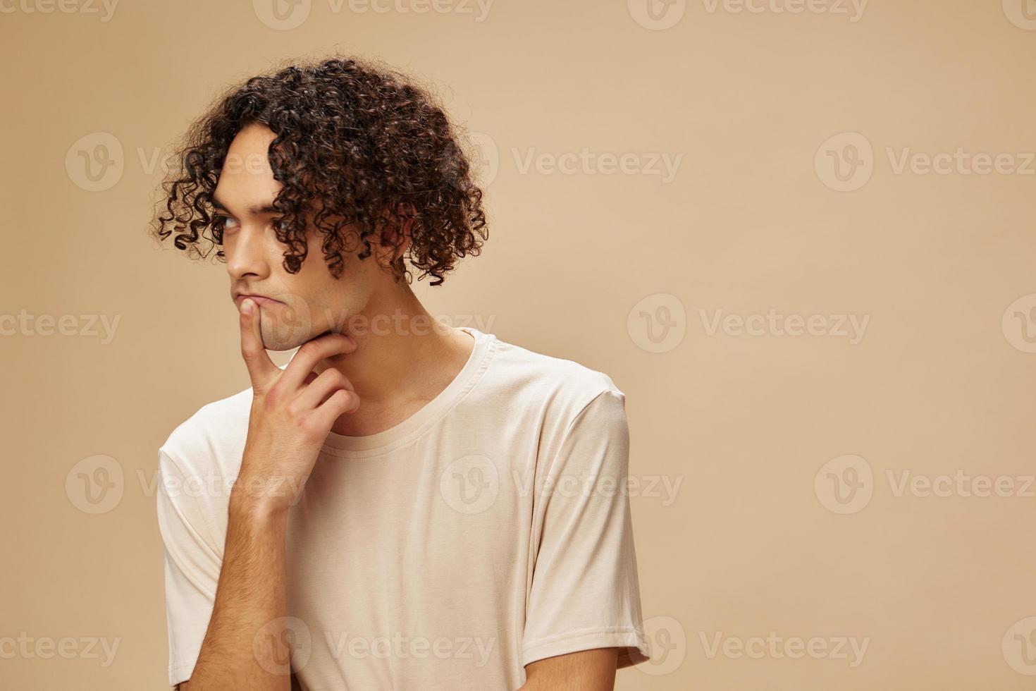 Pensive funny awesome tanned curly man in basic t-shirt can not make decision posing isolated on beige pastel background. Fashion New Collection offer. People and Emotions concept. Free place for ad photo