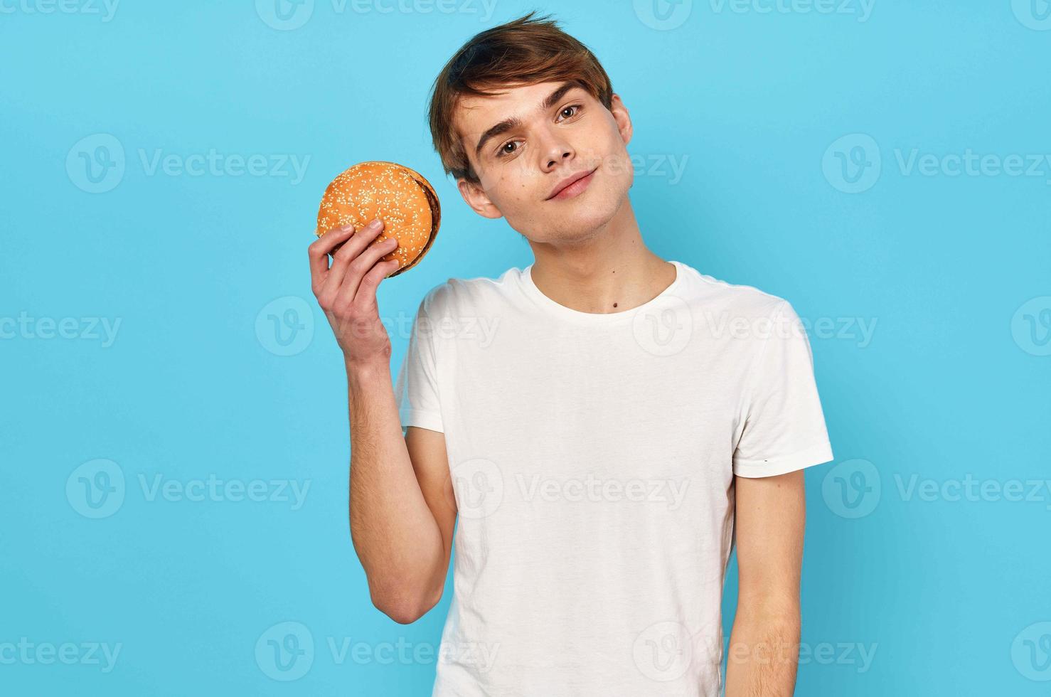 Man eating hamburger in white t-shirt diet food lifestyle blue background photo