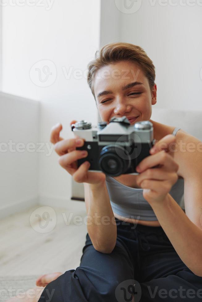 contento sonrisa mujer participación un antiguo cámara y tomando imágenes de sí misma como un fin de semana fotógrafo en hogar ropa con un corto Corte de pelo pelo sin filtros en un blanco fondo, gratis Copiar espacio foto