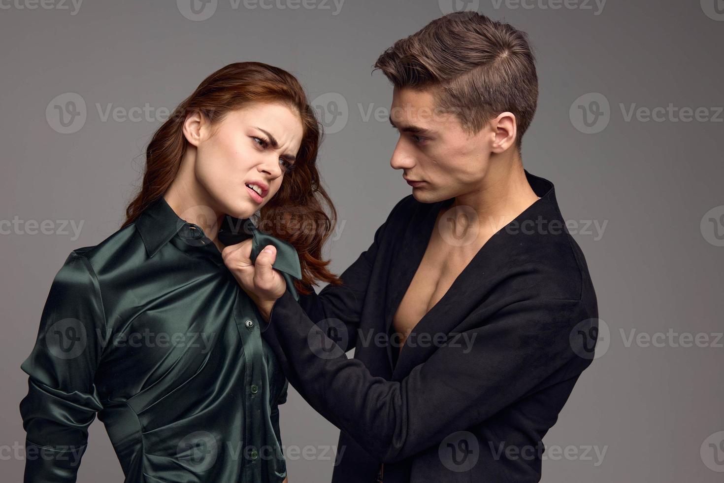 A man holds a woman by the collar causing her pain and on a gray background photo