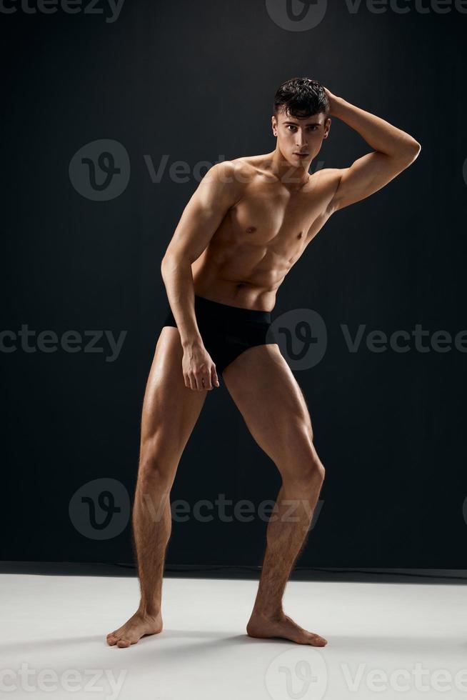 sporty man with muscular naked body in black panties on a dark background photo