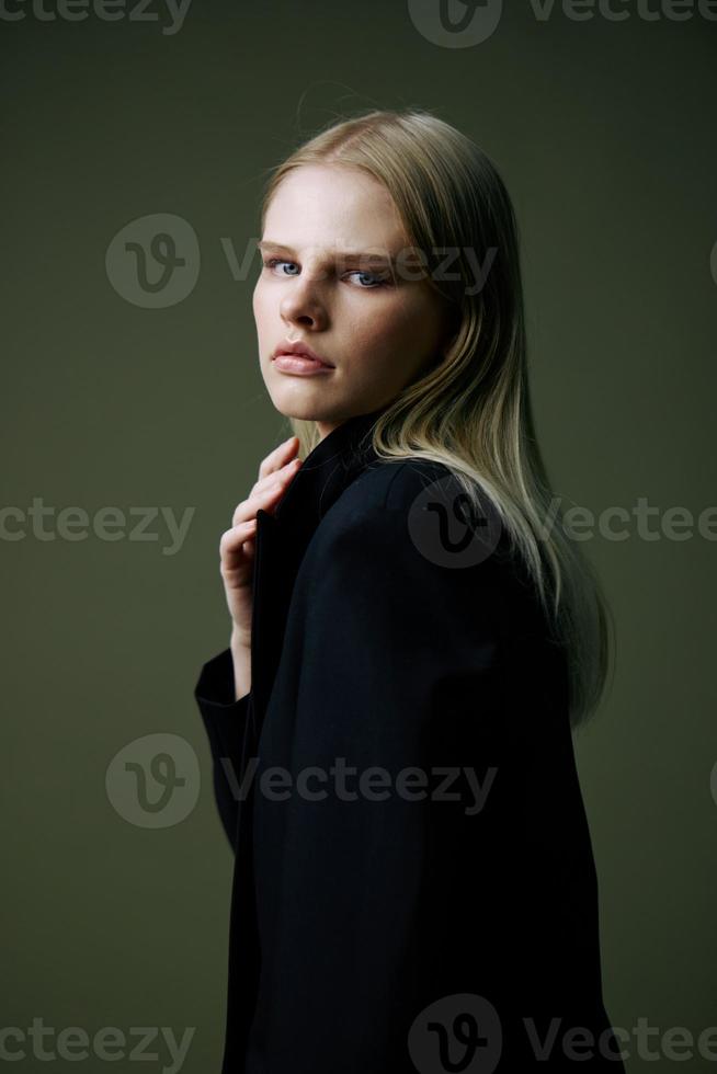 un cerca retrato de un rubia mirando terminado su hombro en un negro chaqueta posando en un estudio en un verde antecedentes. el concepto de elegante Moda fotografía foto