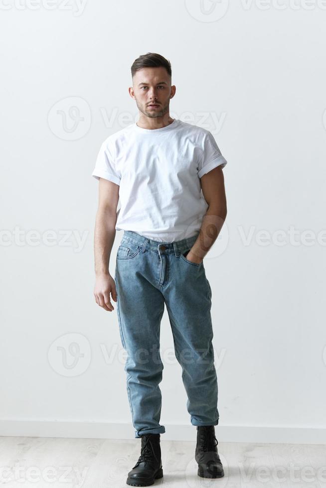 Full body shot of handsome serious tanned man guy in basic t-shirt holds hand on jeans posing on white background. Fashion Style New Collection Offer. Copy space for ad. Modeling snapshots photo