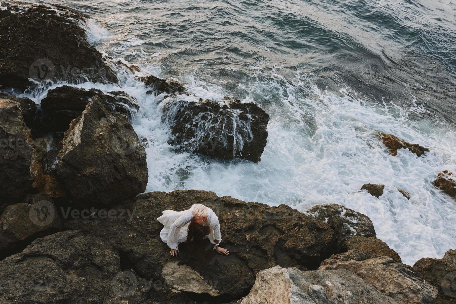 atractivo mujer con largo pelo acostado en rocoso costa con grietas en rocoso superficie inalterado foto