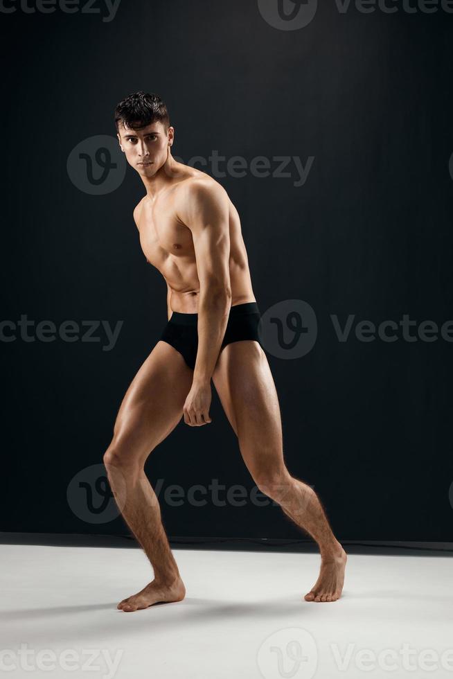 man with muscular naked body in black panties posing against dark background photo