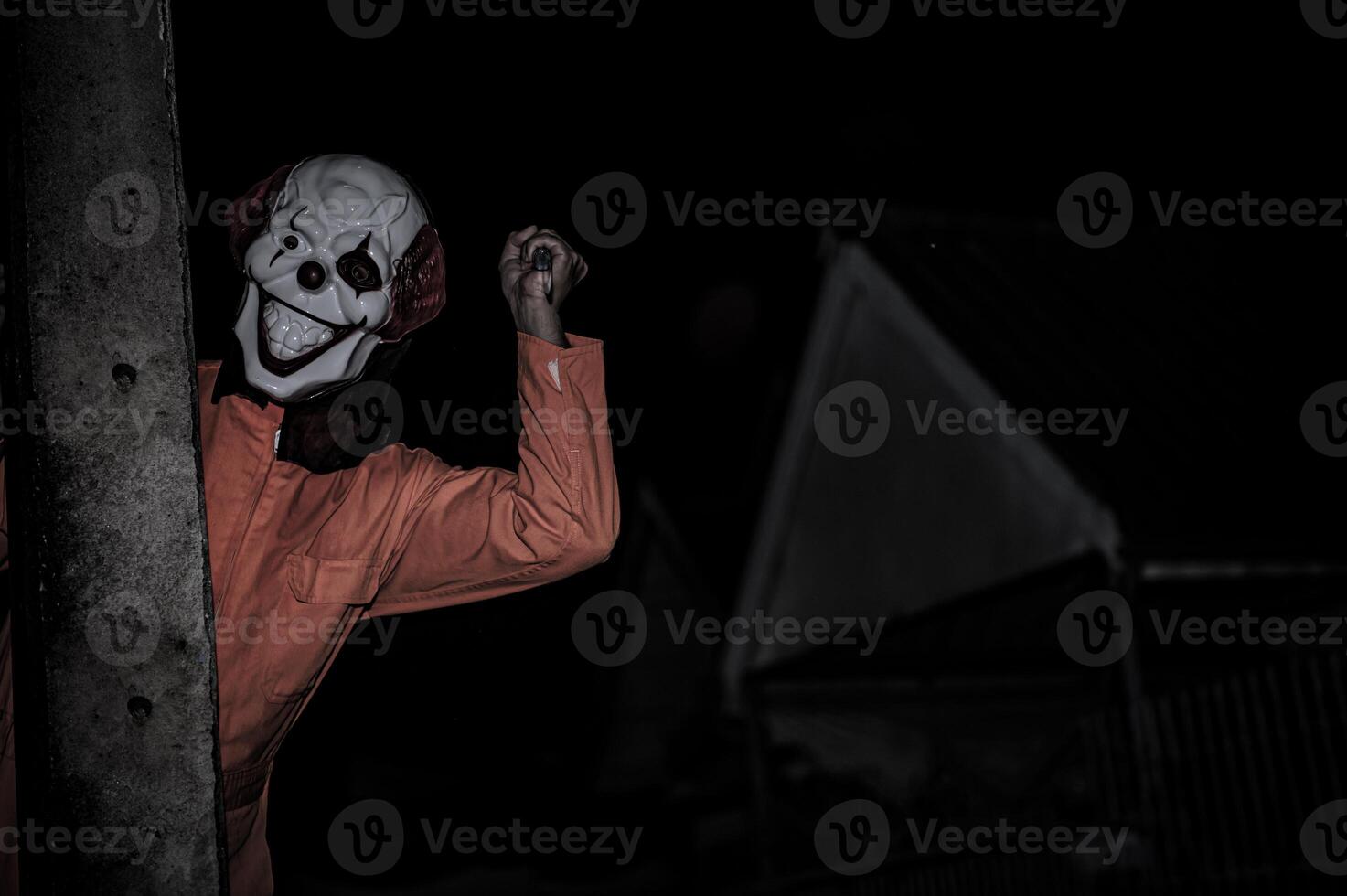 Asian handsome man wear clown mask with weapon at the night scene,Halloween festival concept,Horror scary photo of a killer in orange cloth