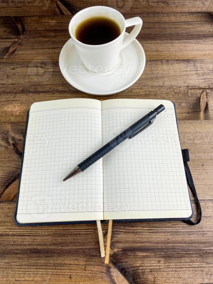 Coffee in a cup and a notebook with a pen. Vertical photo. photo